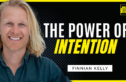 A smiling man with long blonde hair is featured on the left side of the image against a black background with dotted patterns. To the right, bold white and yellow text reads "The Power of Intention," with the name "Finnian Kelly" displayed below. The Chase Jarvis LIVE Show logo is positioned in the upper right corner.