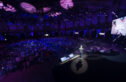 Chase Jarvis on stage at The Next Web Conference, addressing a large audience in a dimly lit auditorium with purple lighting. The audience is seated, attentively listening to the presentation. The stage is equipped with large screens displaying slides, and the venue has a modern, high-tech atmosphere.